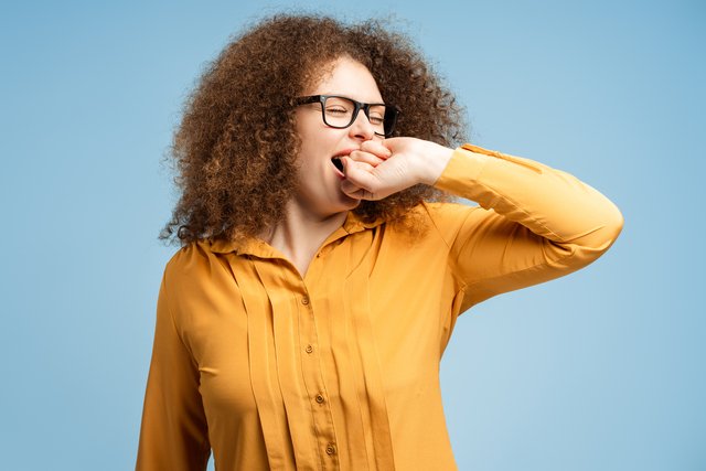 Tired young woman wearing glasses yawning, standing isolated on blue background. Morning concept CPAP-Expert-Clinic-Patient