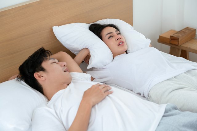 Couple Sleeping in Bed With One Partner Snoring Loudly in a Bright Room CPAP-Expert-Clinic-Snoring